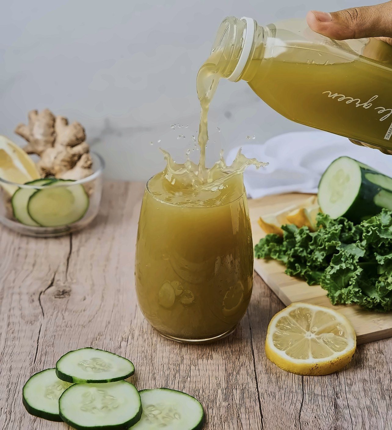 Green juice poured into a glass beside cucumber and kale